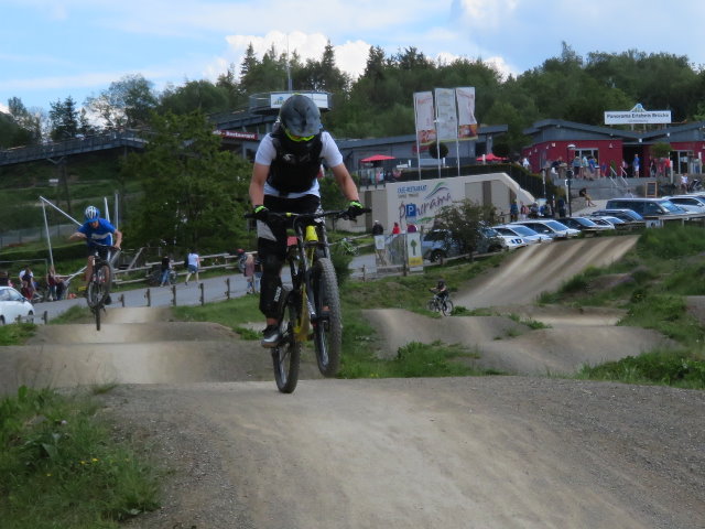 Eine Strecke im Bikepark Winterberg, auf der zwei Biker*innen Tricks vorführen. Der Bikepark Winterberg ist die Austragungsstätte des iXS Dirt Masters Festivals.